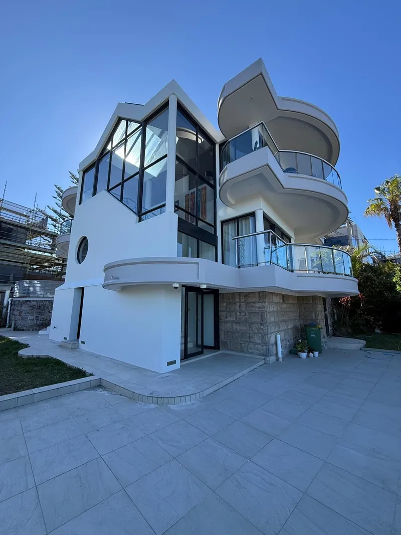 Three-storey white home with curved balconies seen from the paved courtyard