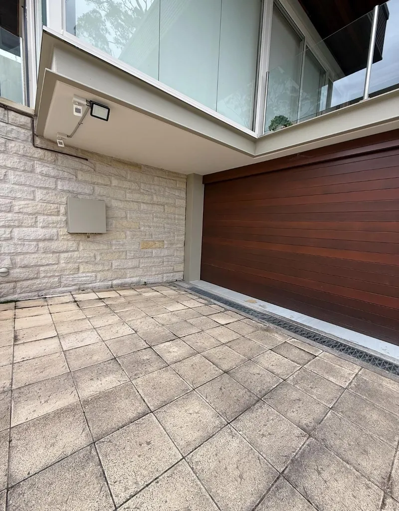 Sandstone wall and timber garage door below a glass balcony
